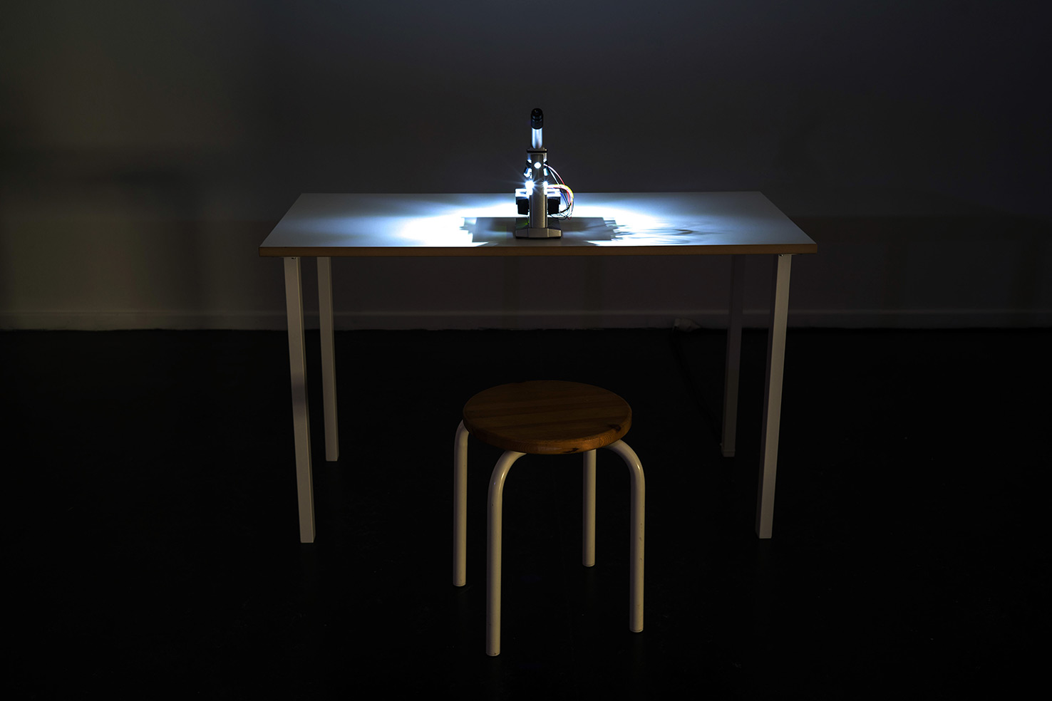 a illuminated microscope on a table with a chair in a dark exhibition space