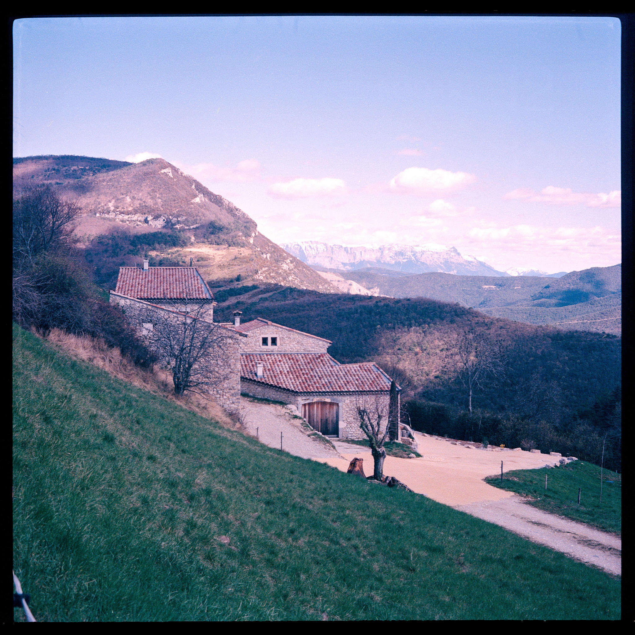 a farm house sourrounded by fresh grass, mountains and clouds