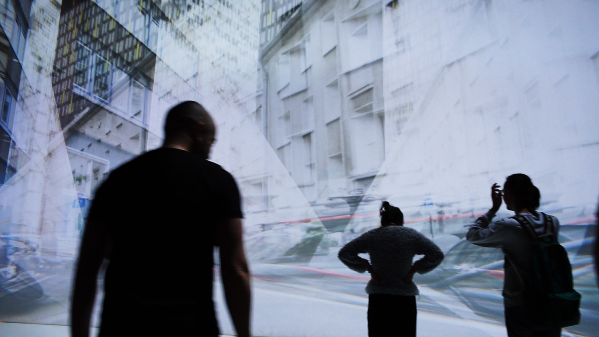  three people in front of projection with multiexposure of buildings viewed from different angles