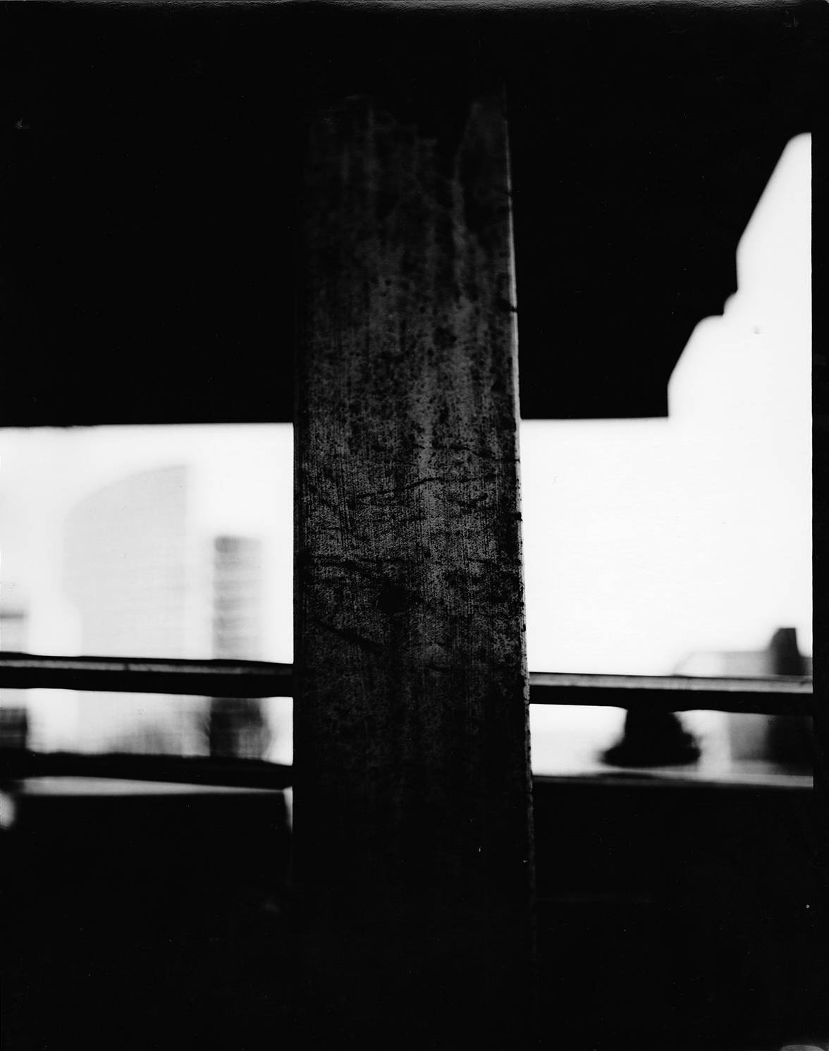 concrete column with blurry buildings in background in high contrast analog black and white