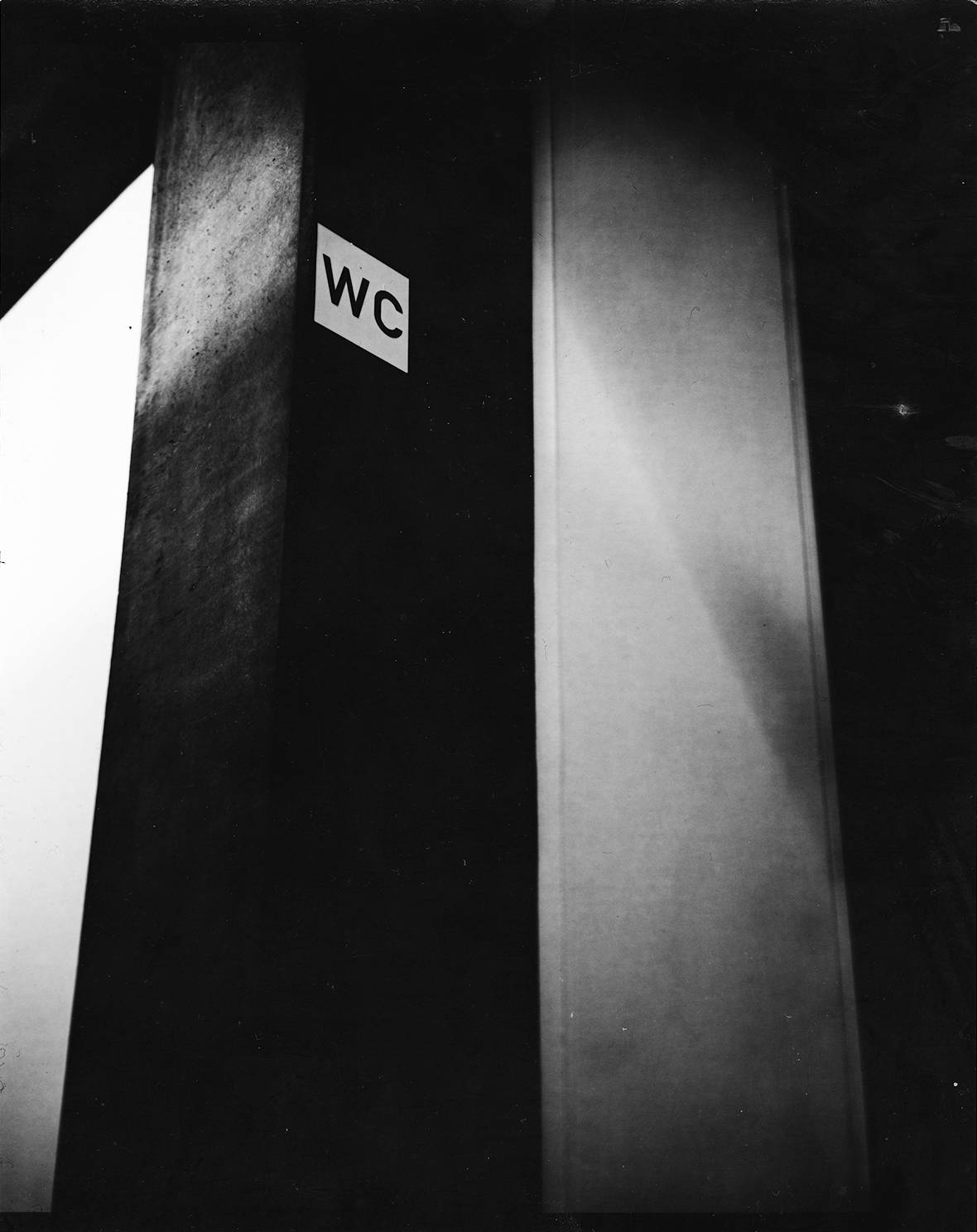a 'WC'-sign on a concrete column in high contrast analog black and white